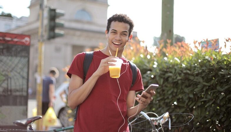 A young man listening to music on his headphones and having an orange juice.